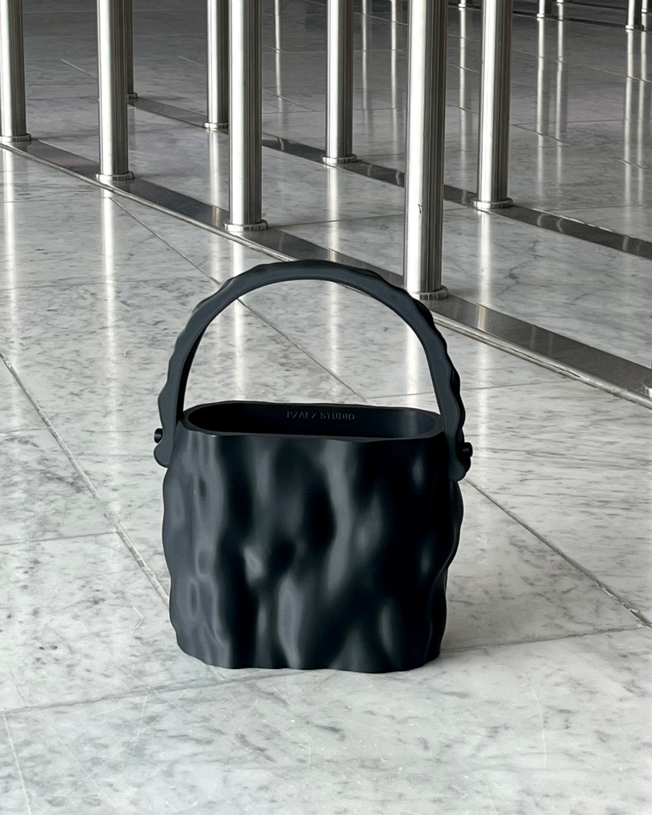 MELT Obsidian black sculptural handbag placed on a marble floor with metal columns in the background.