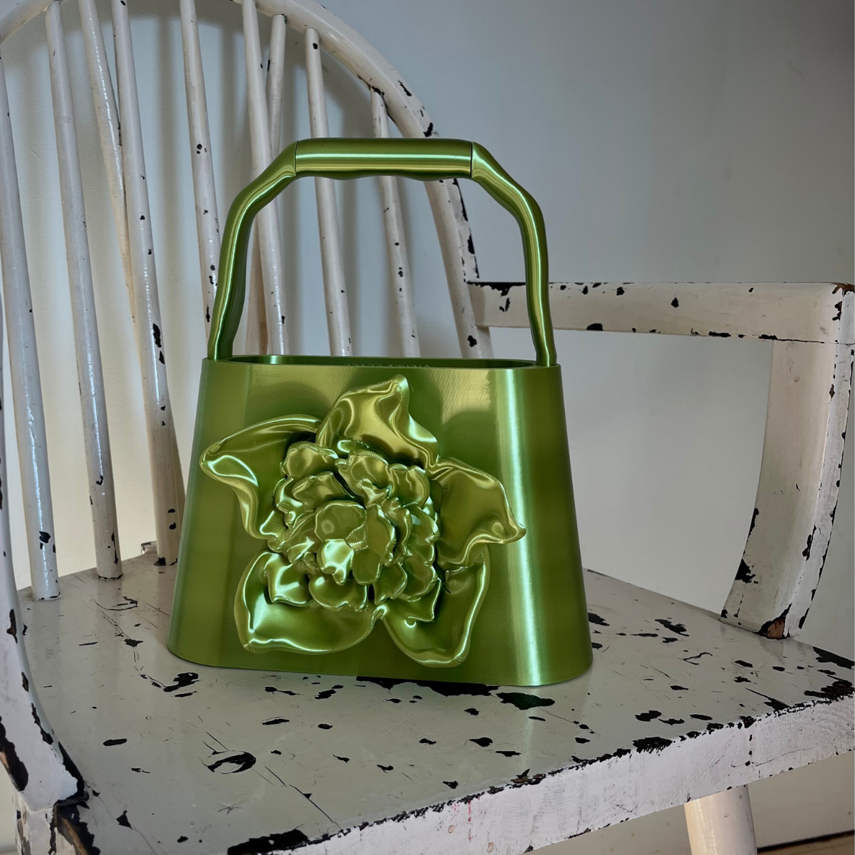 BLOOM bag in Acid Green placed on a worn white chair, showing the sculptural flower detail and metallic surface.