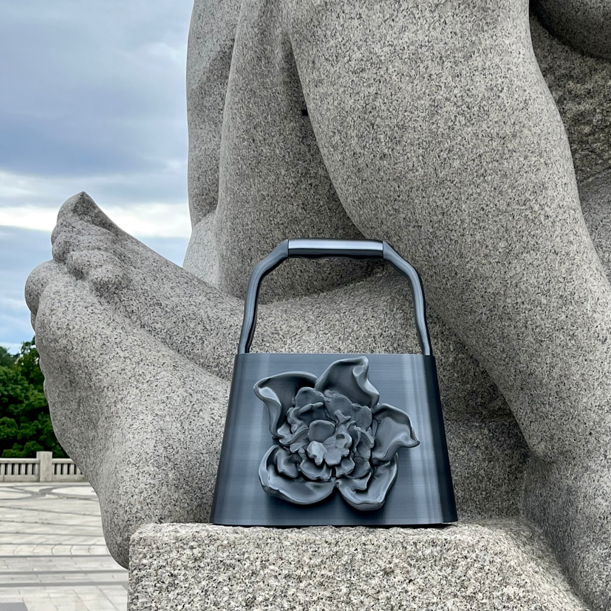 BLOOM bag in Graphite placed on stone sculpture outdoors, showing the sculptural flower detail and structured handle.