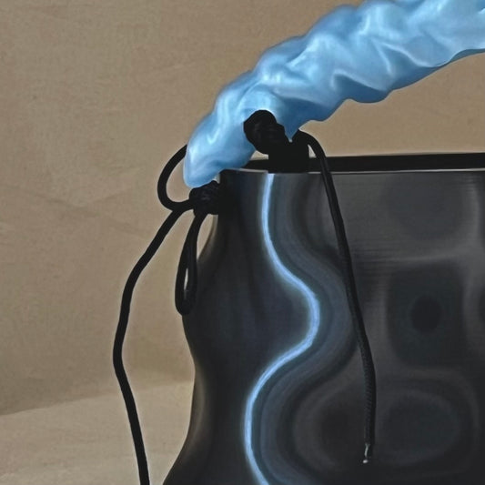 Close-up of LIQUID bag in Onyx Ice, showing the translucent sculptural handle, cord attachment and reflective surface detail.