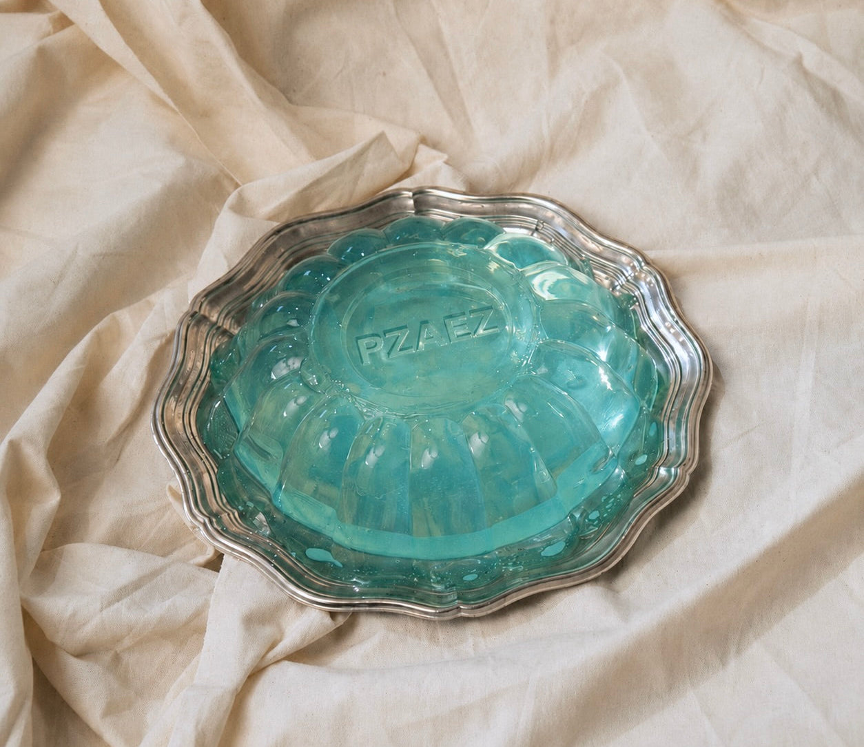 Translucent blue PZAEZ object placed on draped beige fabric